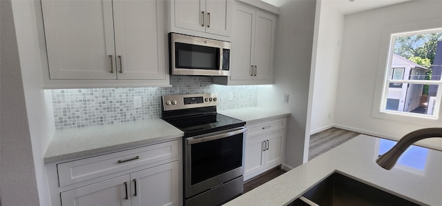 kitchen featuring hardwood / wood-style floors, sink, stainless steel appliances, white cabinets, and decorative backsplash