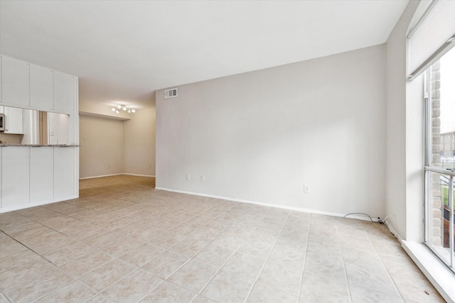 unfurnished room featuring a healthy amount of sunlight, visible vents, baseboards, and light tile patterned flooring