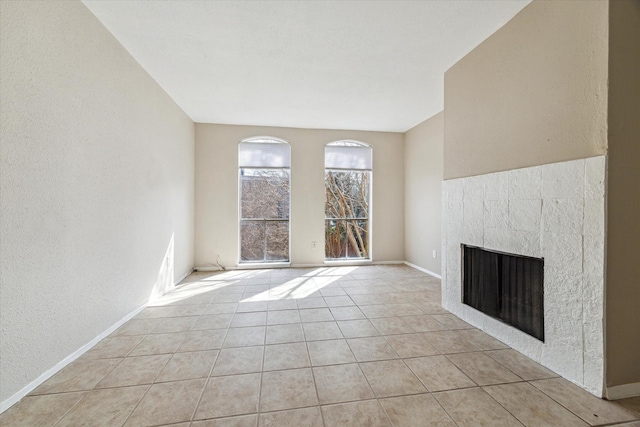 unfurnished living room featuring baseboards, a textured wall, a tiled fireplace, and light tile patterned floors