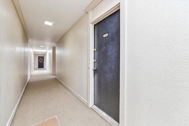 corridor with light carpet, a textured wall, and baseboards