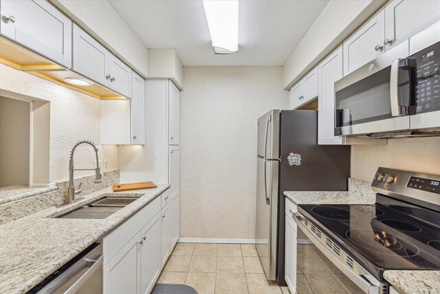 kitchen with stainless steel appliances, a sink, light stone countertops, and white cabinets