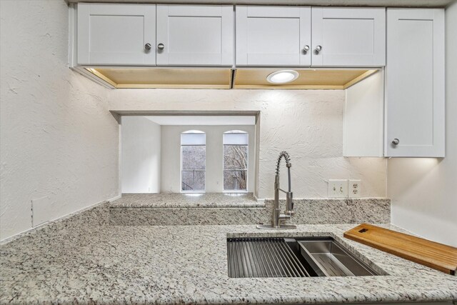 kitchen with a textured wall, light stone counters, a sink, and white cabinets