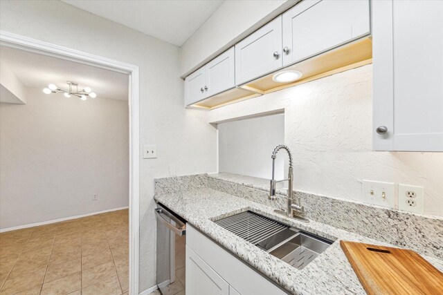 kitchen featuring light stone counters, white cabinets, dishwasher, and a sink