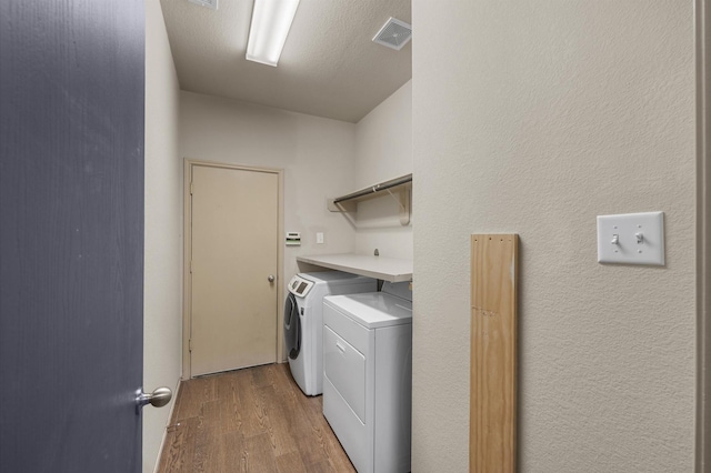 laundry room featuring hardwood / wood-style flooring, a textured ceiling, and washing machine and clothes dryer