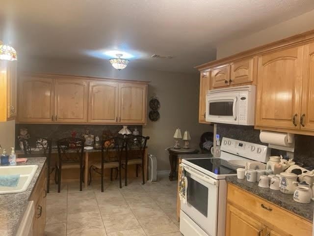 kitchen with sink, white appliances, dark stone counters, and light tile patterned floors