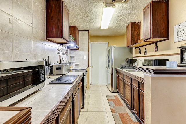 kitchen featuring sink, light tile patterned flooring, a textured ceiling, tile counters, and decorative backsplash