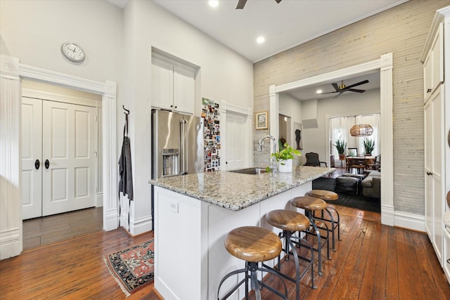 kitchen featuring a center island with sink, a kitchen bar, sink, white cabinets, and light stone countertops