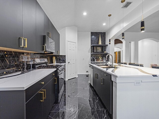 kitchen featuring appliances with stainless steel finishes, decorative light fixtures, decorative backsplash, sink, and a kitchen island with sink