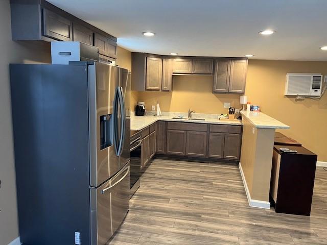 kitchen with an AC wall unit, light hardwood / wood-style floors, stainless steel fridge, sink, and kitchen peninsula