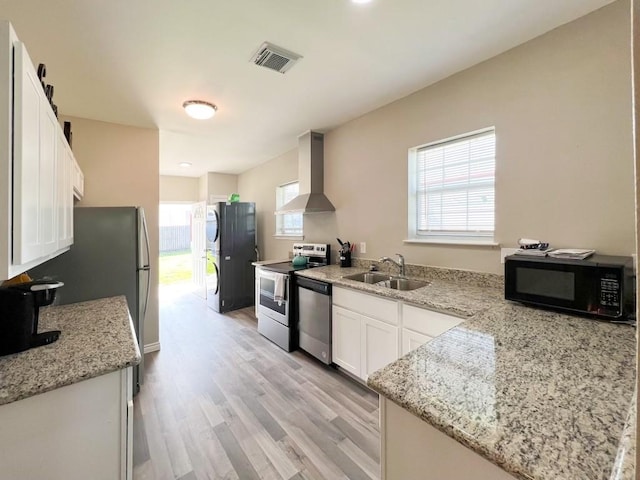 kitchen with black appliances, sink, light stone counters, white cabinets, and wall chimney exhaust hood