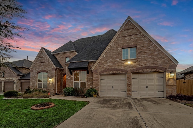 view of front of house featuring a garage, concrete driveway, roof with shingles, a yard, and brick siding