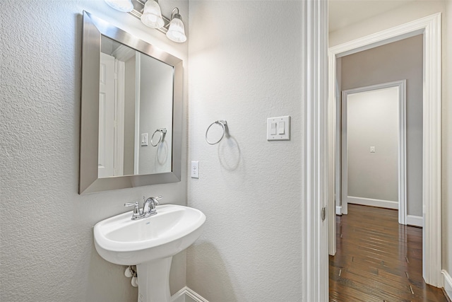 bathroom with a sink, baseboards, wood finished floors, and a textured wall