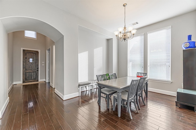 dining space featuring arched walkways, dark wood-type flooring, a chandelier, and baseboards