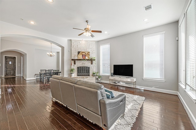 living area with visible vents, dark wood finished floors, arched walkways, a fireplace, and ceiling fan with notable chandelier