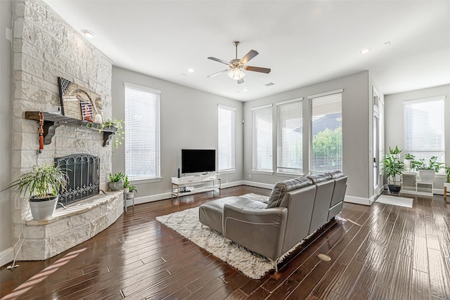 living room with ceiling fan, a stone fireplace, wood finished floors, visible vents, and baseboards