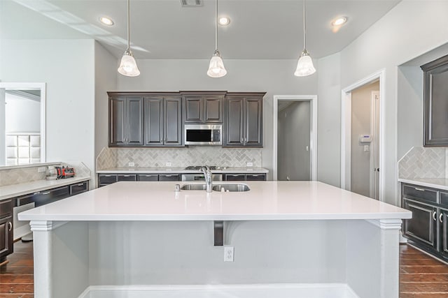 kitchen with light countertops, stainless steel microwave, a sink, and a kitchen island with sink