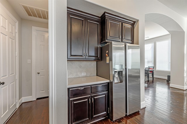 kitchen featuring arched walkways, dark brown cabinetry, dark wood-style flooring, visible vents, and stainless steel refrigerator with ice dispenser