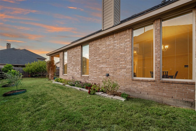 view of home's exterior featuring a yard, a chimney, fence, and brick siding