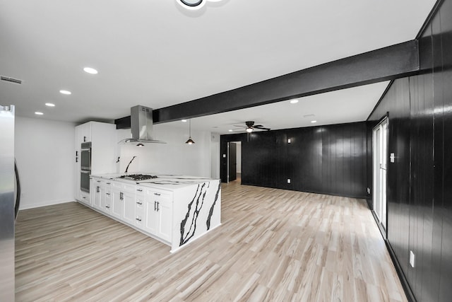 kitchen with beam ceiling, white cabinetry, appliances with stainless steel finishes, and wall chimney range hood