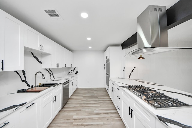 kitchen featuring stainless steel appliances, light stone counters, white cabinets, and range hood