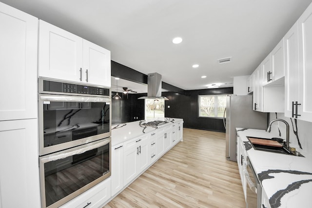 kitchen with sink, appliances with stainless steel finishes, white cabinets, and island range hood