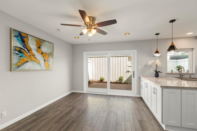 kitchen featuring light stone counters, pendant lighting, dark hardwood / wood-style flooring, sink, and white cabinetry