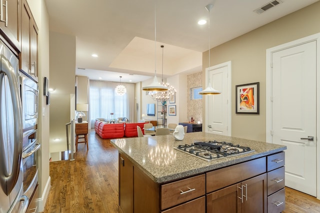 kitchen with hanging light fixtures, stainless steel appliances, a center island, a tray ceiling, and dark wood-type flooring