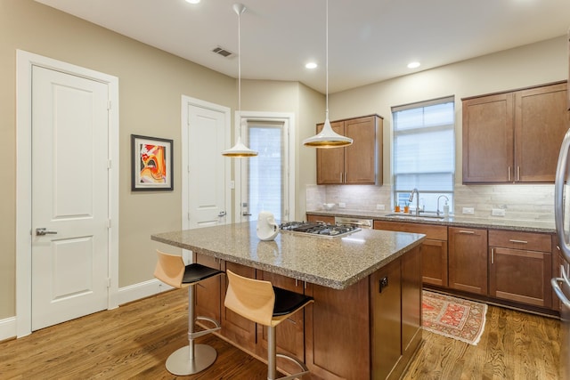 kitchen with a breakfast bar, sink, pendant lighting, a kitchen island, and light stone countertops