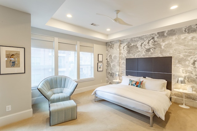 carpeted bedroom with ceiling fan and a raised ceiling