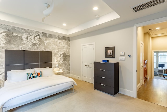 bedroom with light carpet and a tray ceiling