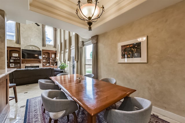 dining area with light tile patterned floors, baseboards, a raised ceiling, a fireplace, and a chandelier