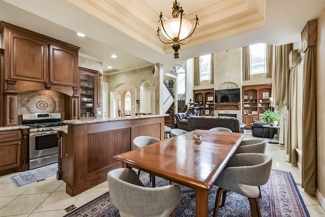 dining area featuring a tray ceiling, crown molding, a fireplace, stairway, and light tile patterned flooring