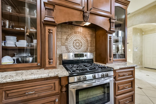 kitchen with stainless steel range oven, glass insert cabinets, and light stone countertops