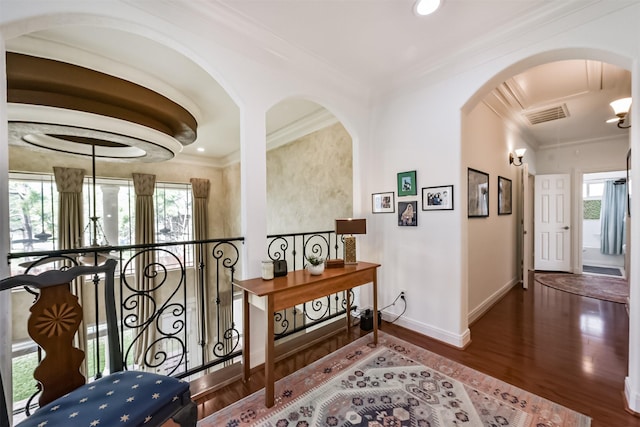 hallway featuring baseboards, visible vents, arched walkways, wood finished floors, and crown molding