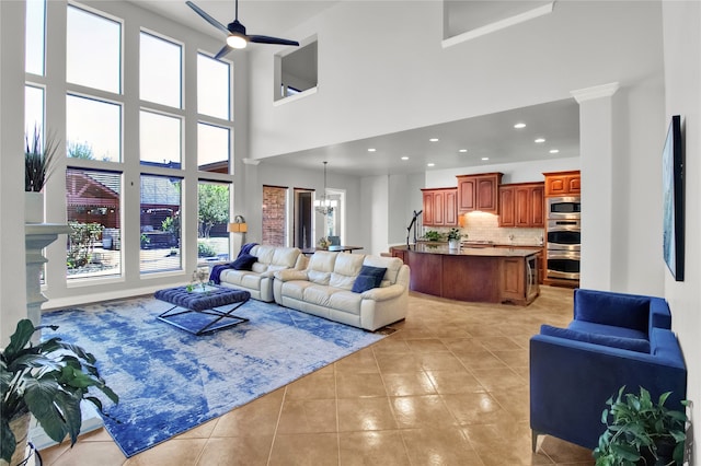 tiled living room featuring a high ceiling and ceiling fan with notable chandelier