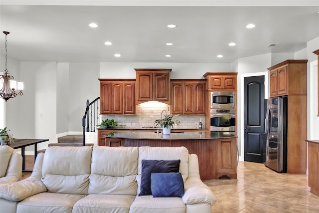 kitchen featuring appliances with stainless steel finishes, backsplash, a notable chandelier, pendant lighting, and an island with sink