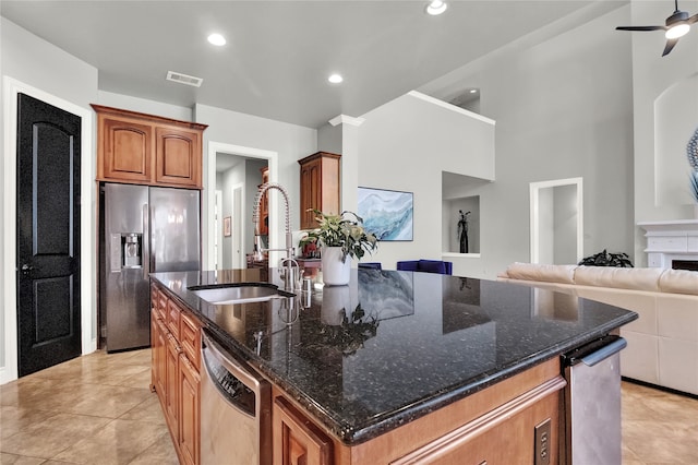 kitchen featuring dark stone countertops, appliances with stainless steel finishes, sink, an island with sink, and a high ceiling