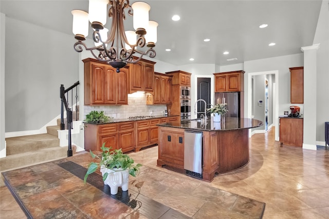 kitchen with a kitchen island with sink, stainless steel appliances, decorative light fixtures, sink, and decorative backsplash