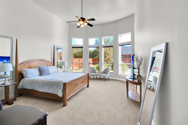 bedroom with ceiling fan, light colored carpet, and a towering ceiling