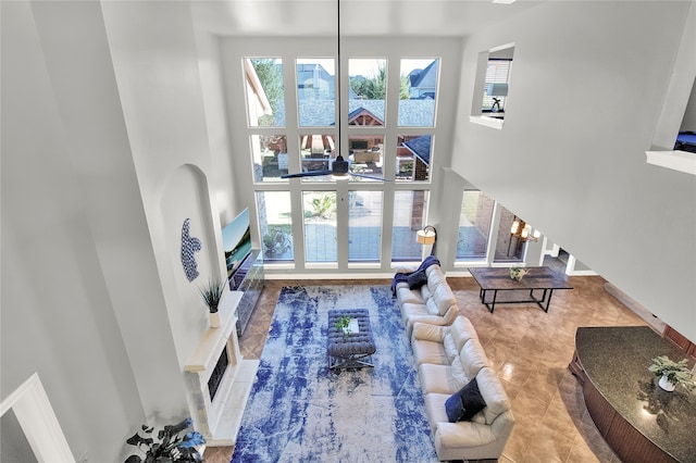 tiled living room featuring a fireplace, ceiling fan, a towering ceiling, and a healthy amount of sunlight