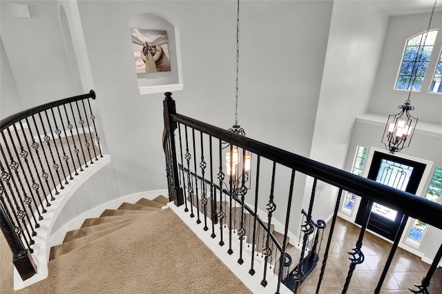 stairway featuring tile patterned flooring, a towering ceiling, and an inviting chandelier