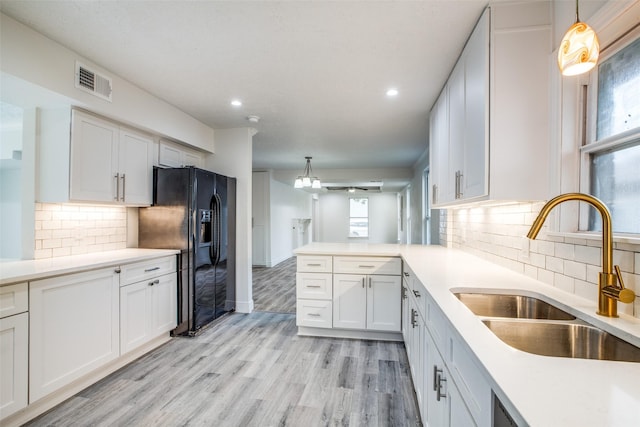 kitchen with white cabinetry, pendant lighting, sink, black fridge, and kitchen peninsula