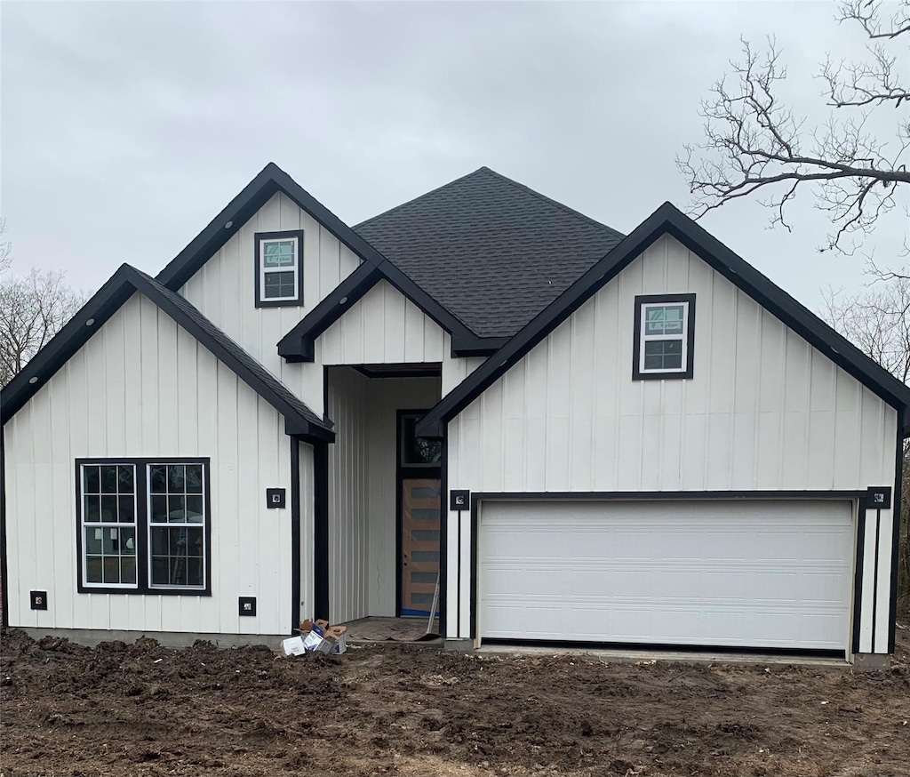 modern inspired farmhouse featuring dirt driveway, a shingled roof, board and batten siding, and an attached garage