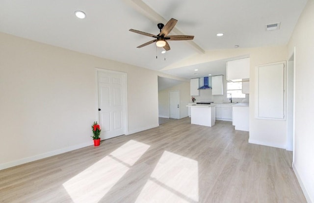 unfurnished living room featuring sink, ceiling fan, light hardwood / wood-style floors, and lofted ceiling with beams