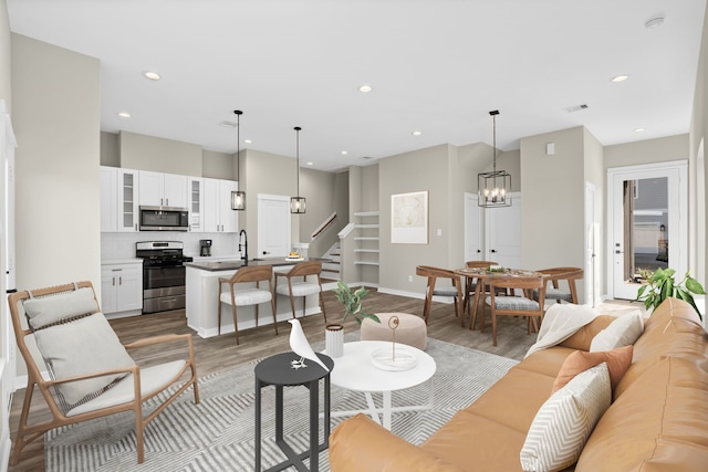 living room featuring recessed lighting, wood finished floors, baseboards, stairway, and an inviting chandelier