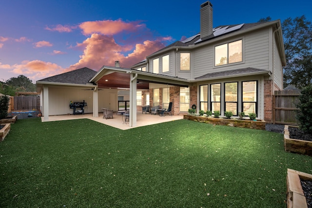 back house at dusk featuring a patio, solar panels, and a yard