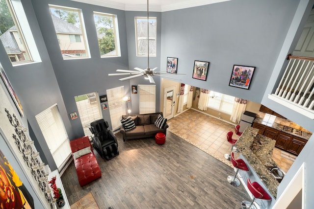 living room featuring ceiling fan, crown molding, wood-type flooring, and a towering ceiling