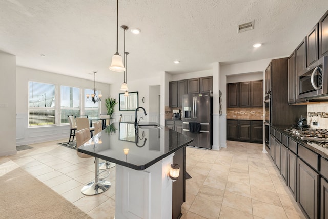 kitchen with appliances with stainless steel finishes, an island with sink, dark brown cabinetry, pendant lighting, and sink