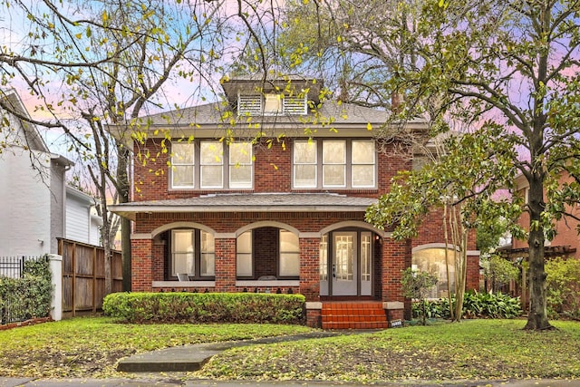 american foursquare style home featuring a front yard, fence, and brick siding