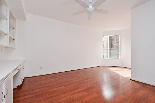 unfurnished room with dark wood-type flooring, built in desk, and ceiling fan